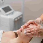 A medical aesthetics specialist analyzing a client's skin tone during a facial treatment consultation.