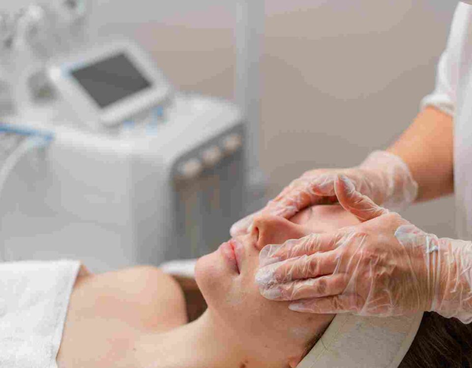 A medical aesthetics specialist analyzing a client's skin tone during a facial treatment consultation.